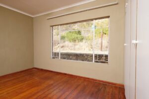 Bright empty bedroom with a large window and wooden floor, ideal for home decor or real estate listings.